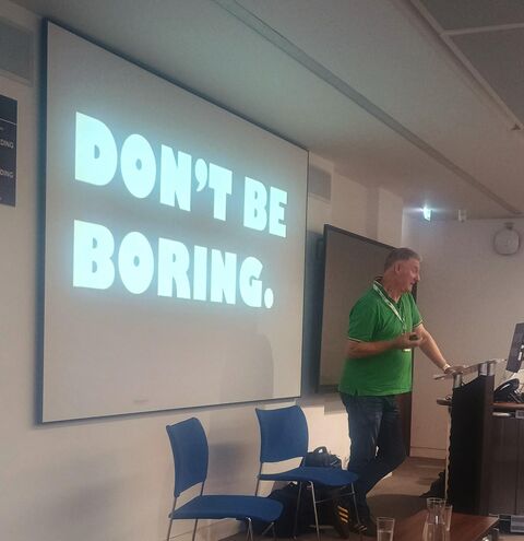 Gerry Farrell presenting a bold slide with the phrase “DON’T BE BORING”.